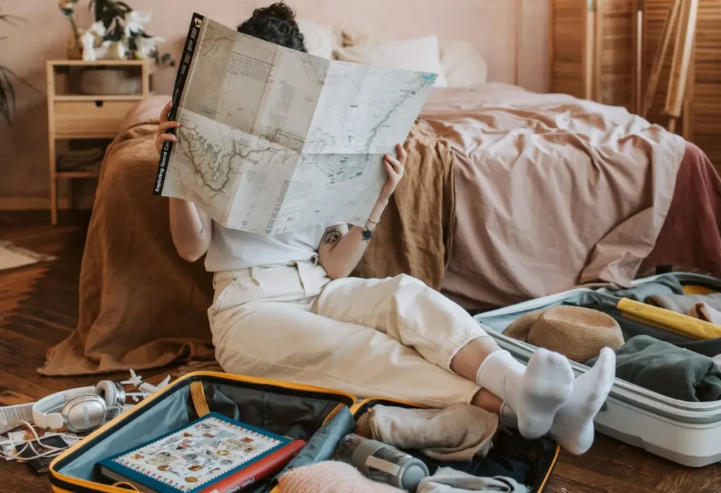 Imagem: Mulher segurando um mapa com as malas no chão e planejando uma viagem.