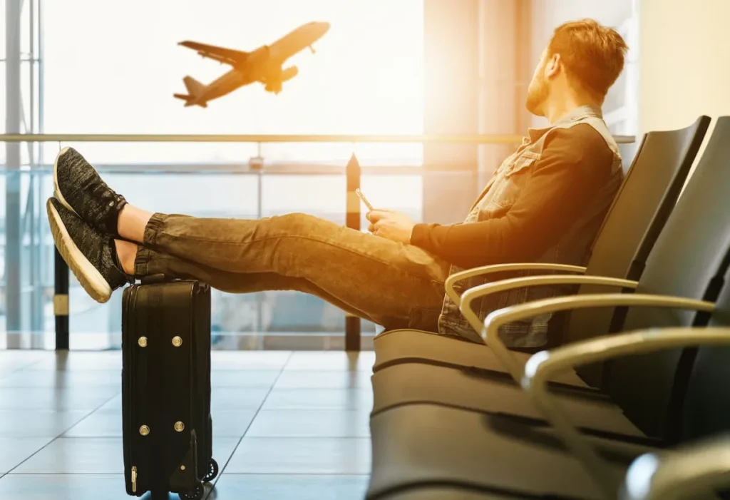 imagem: Um homem sentado no aeroporto olhando um avião decolar. A imagem ilustra dicas de segurança para uma viagem tranquila.