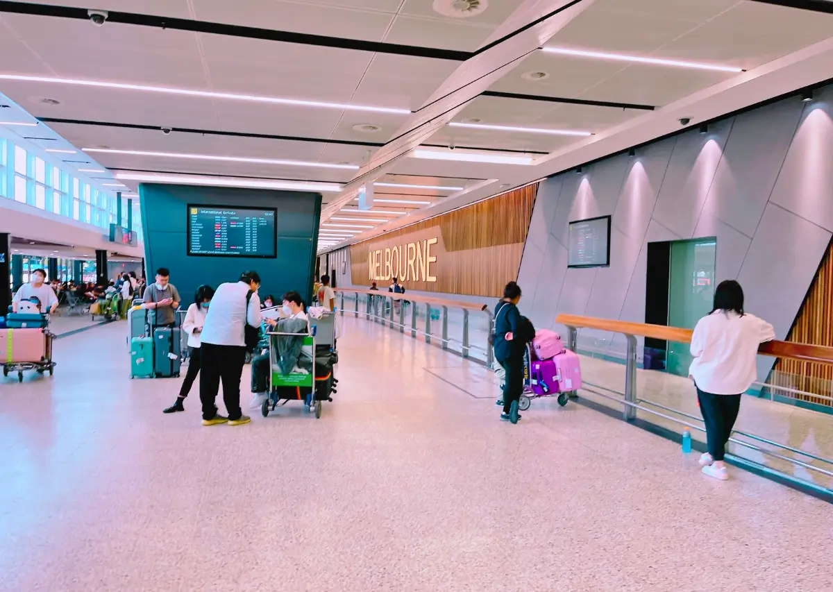 Interior do aeroporto de Melbourne, com passageiros e placas de informação.