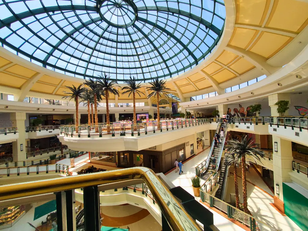 Interior do Shopping Iguatemi Campinas, com uma ampla cúpula de vidro, palmeiras decorativas e escadas rolantes, mostrando áreas de lojas e visitantes.