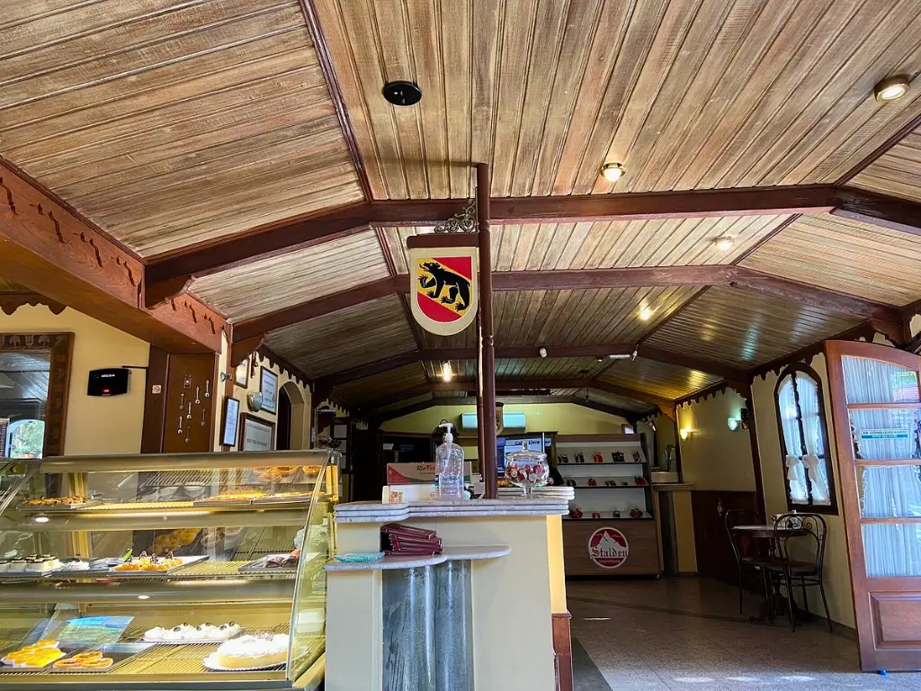 Interior da Stalden Chocolates com teto de madeira rústica, balcão de vidro exibindo sobremesas, decoração com escudo e iluminação suave, criando um ambiente acolhedor e tradicional.