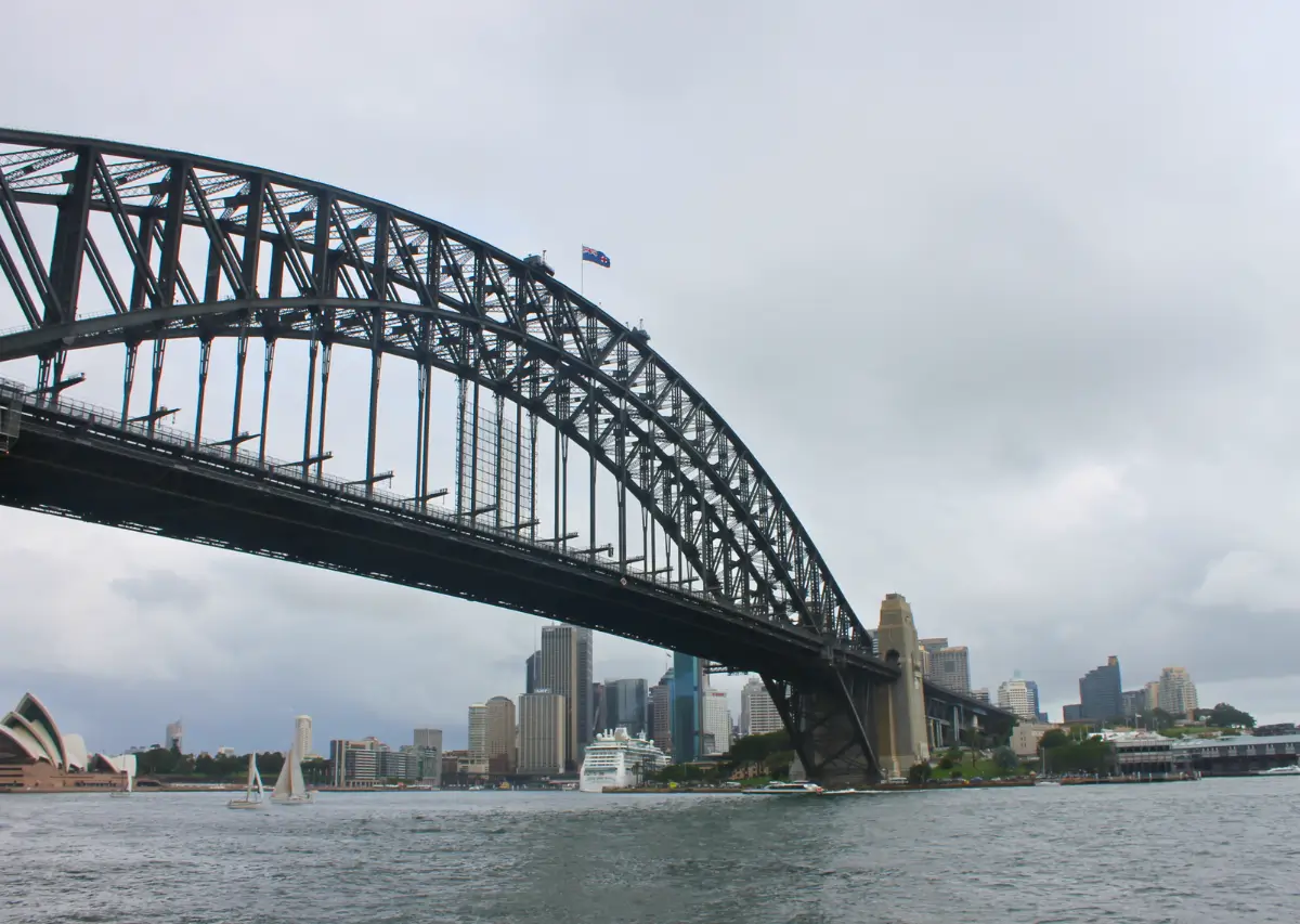 Vista do Sydney Harbour Bridge em um dia nublado, com a Sydney Opera House e a cidade de Sydney ao fundo.