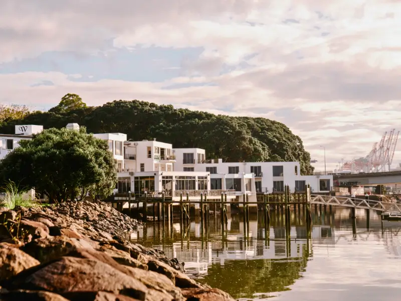 Vista pacífica de apartamentos modernos ao longo da orla com árvores frondosas e reflexo na água, em Tauranga.