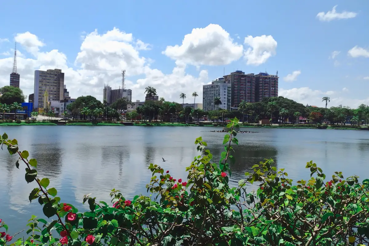 Vista do parque com lago em João Pessoa, prédios ao fundo sob céu azul.
