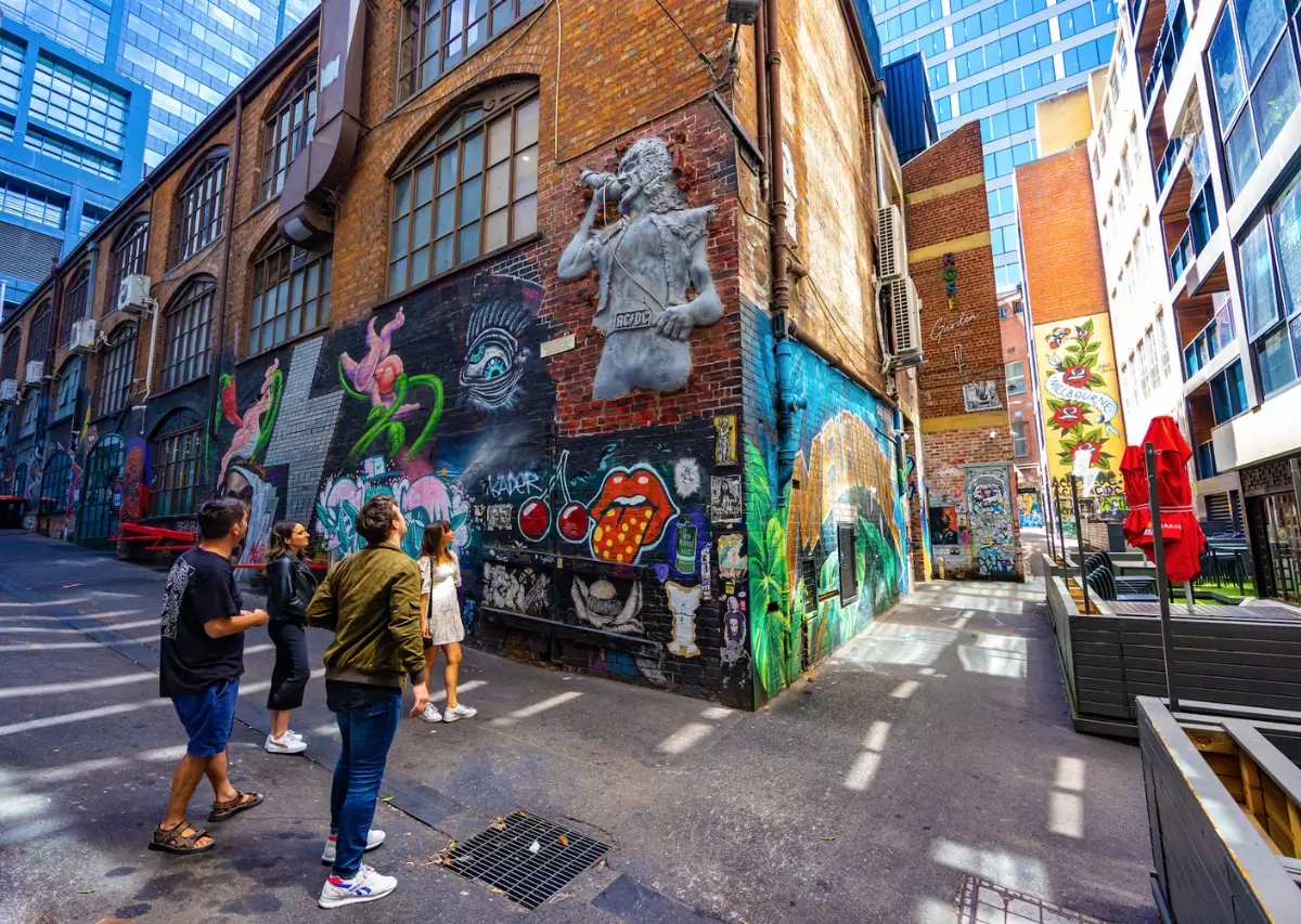 Pessoas admirando arte de rua colorida em um beco de Melbourne, com murais vibrantes e esculturas.

