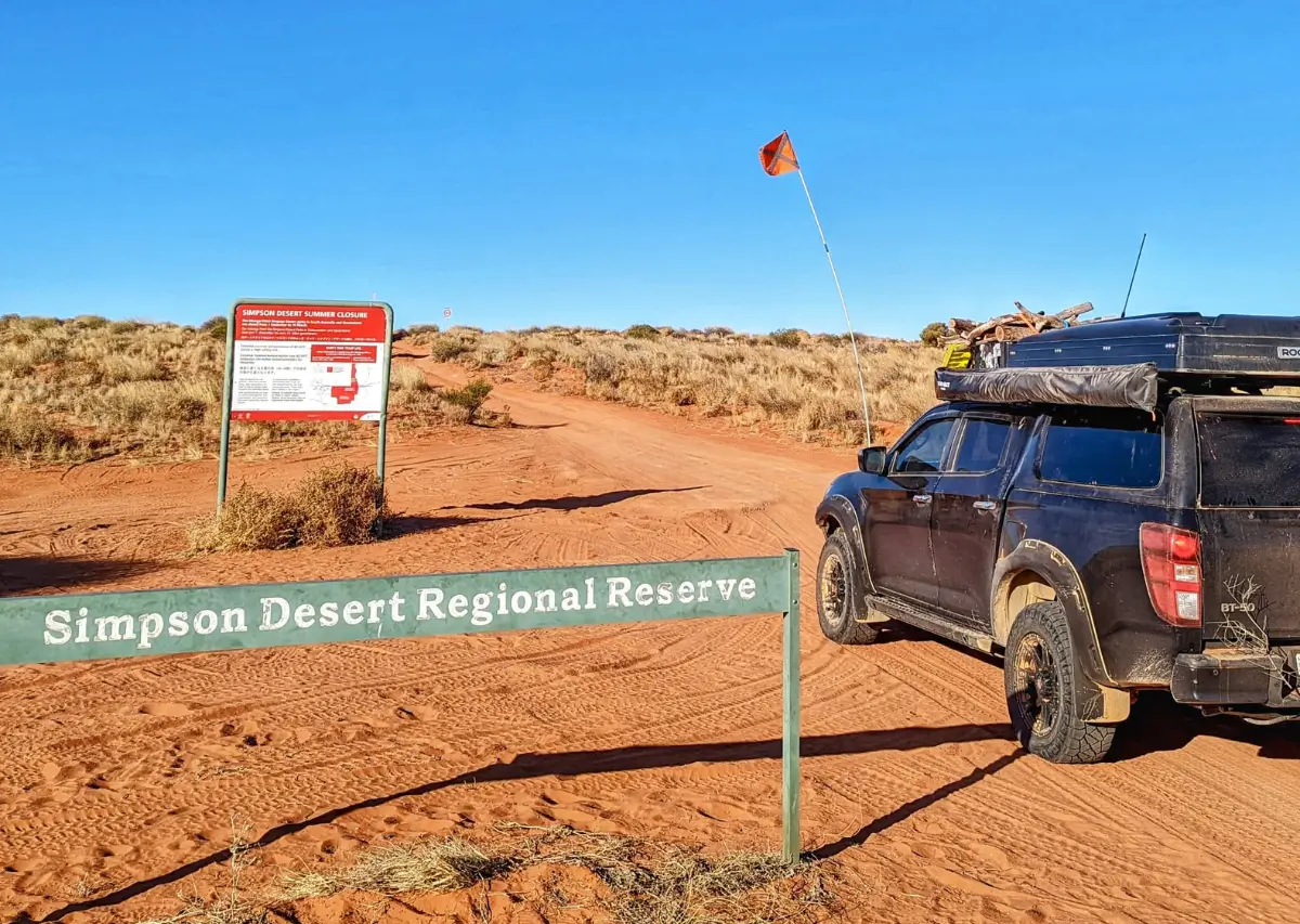 Um veículo off-road estacionado na entrada da Reserva Regional do Deserto de Simpson, com sinalização informativa e uma paisagem árida ao fundo.