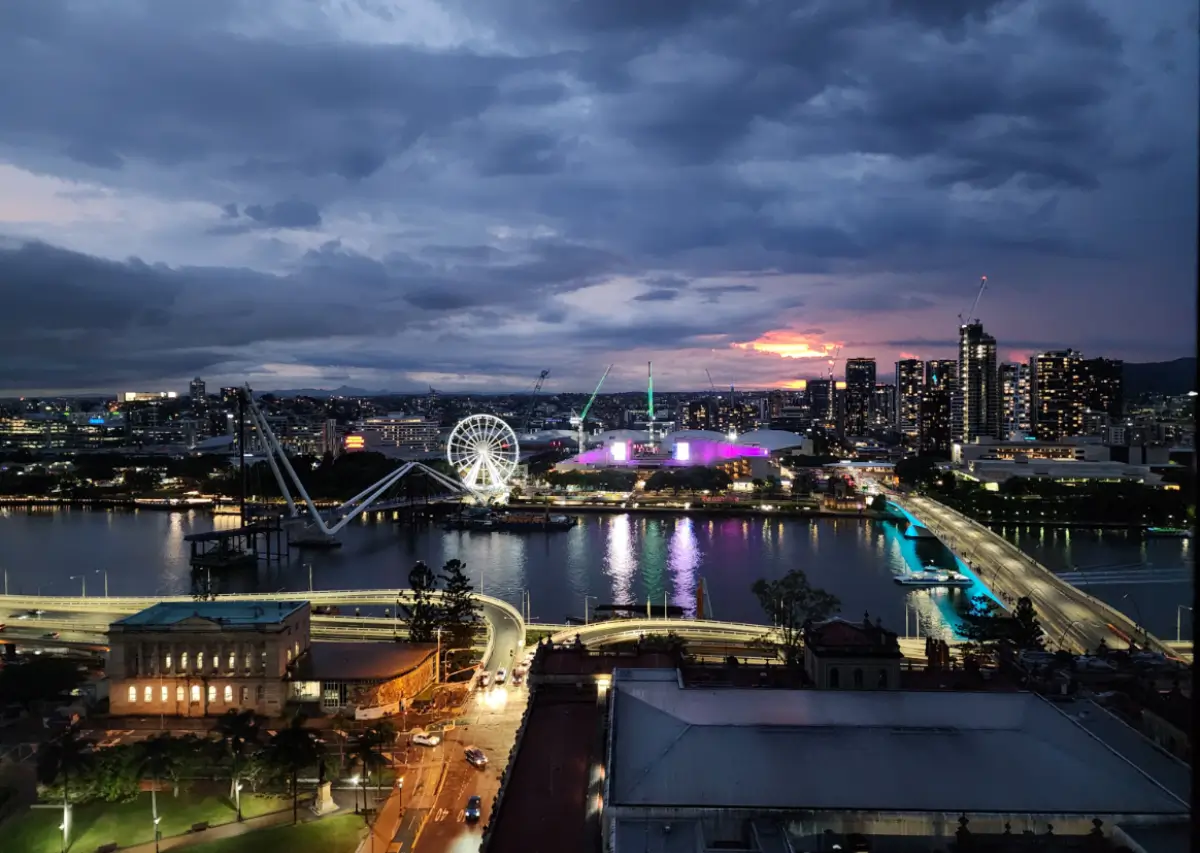 Vista noturna de Brisbane com a roda-gigante iluminada e a cidade refletida no rio.